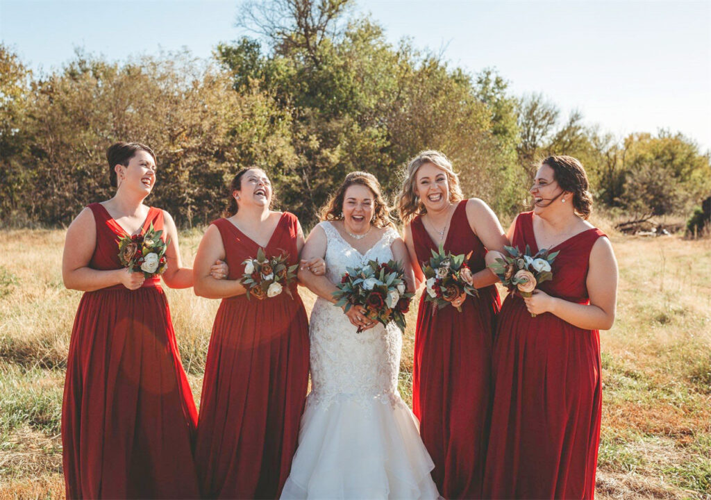 A bride and a group of bridesmaids laughing happily in the forest, wearing AW dresses.