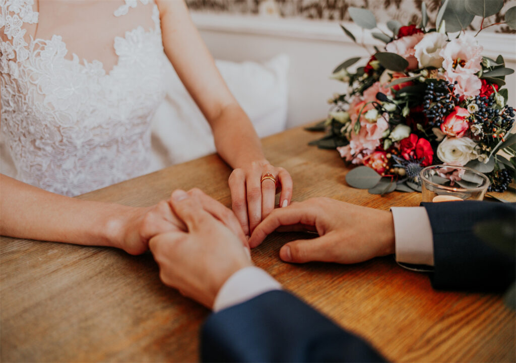 A bride and a groom are holding hands, with pretty flowers surrounded by them.