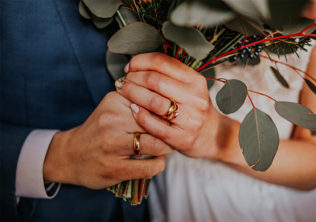 The groom and the bride have their hands crossed, each other has a wedding ring on her hand, they feel happy.