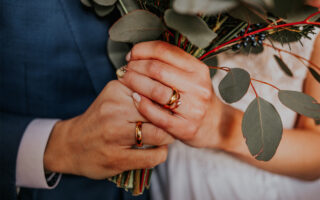 The groom and the bride have their hands crossed, the bride has a wedding ring on her hand, they feel happy.