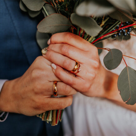 The groom and the bride have their hands crossed, the bride has a wedding ring on her hand, they feel happy.