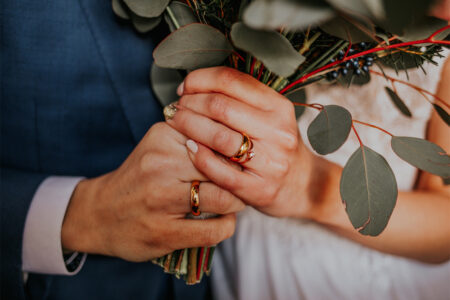 The groom and the bride have their hands crossed, the bride has a wedding ring on her hand, they feel happy.