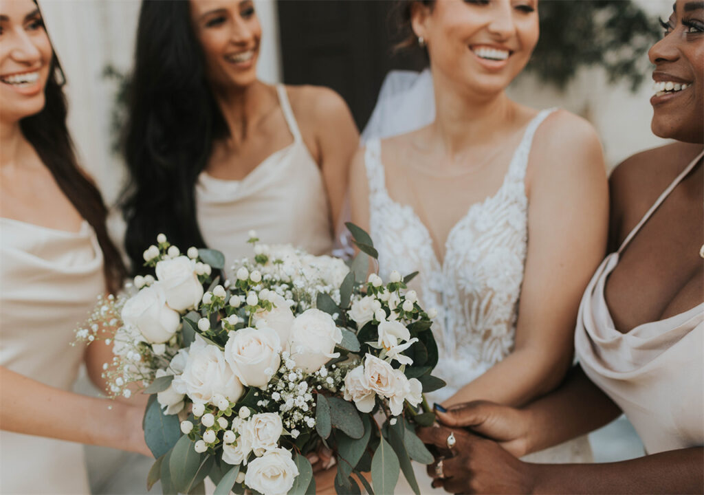 The bride and her bridesmaids are holding a bunch of flowers and laughing together in the wedding party.