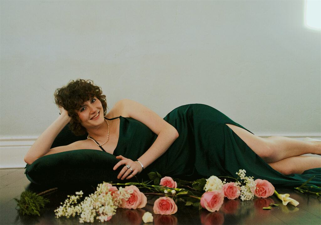 A woman who wears AW Bridal bridesmaid dress is lying on the ground, with flowers by her side.