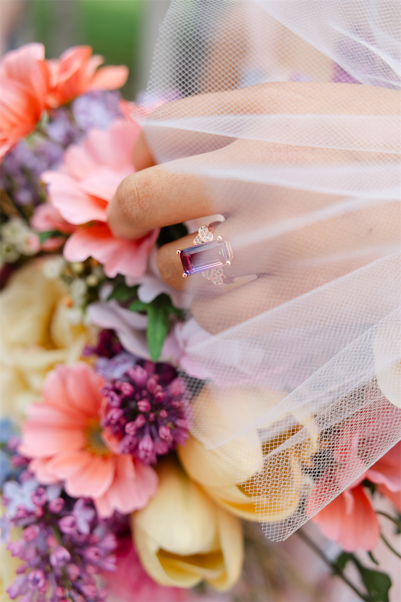  A bride with a gemstone wedding ring gently touches the petals of a flower with her delicate hand.