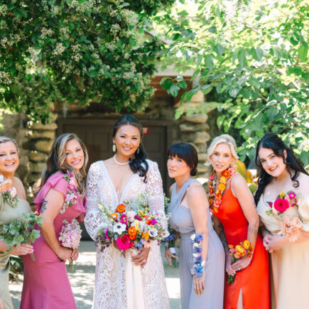 A group of beautiful women, holding flowers, are smiling radiantly in the sunlight.