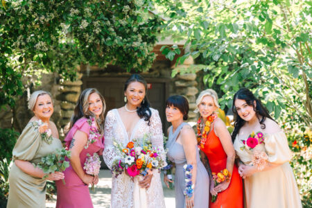 A group of beautiful women, holding flowers, are smiling radiantly in the sunlight.