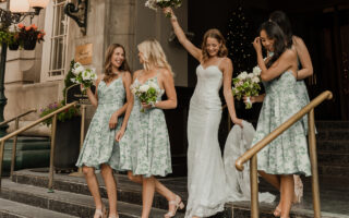 Bride flanked by bridesmaids in green floral dresses, all holding bouquets and smiling