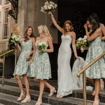 Bride flanked by bridesmaids in green floral dresses, all holding bouquets and smiling