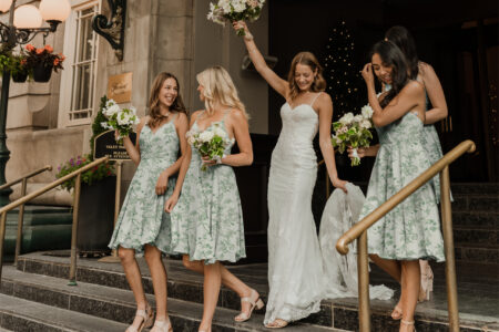 Bride flanked by bridesmaids in green floral dresses, all holding bouquets and smiling