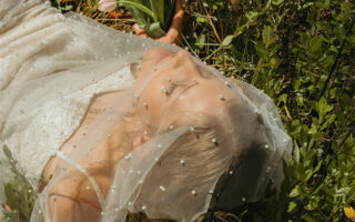 Woman in a wedding dress lying in grass, holding a bouquet of pink tulips.