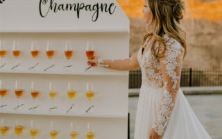 A bride standing next to rows of champagne flutes, holding one in her hand.