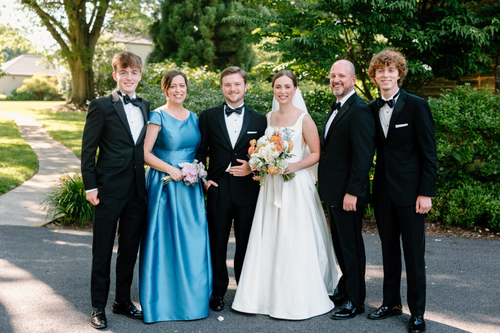 A bride and groom with their family in formal attire, posing outdoors.