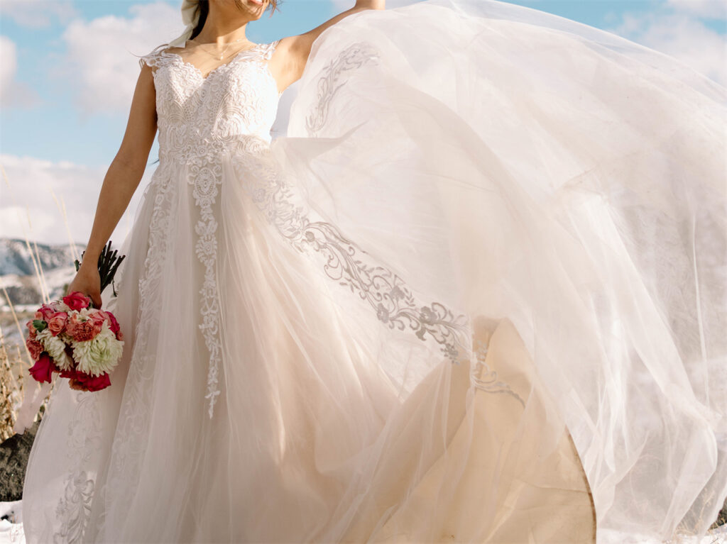 Detailed lace wedding gown flowing in the wind with a bouquet of flowers.