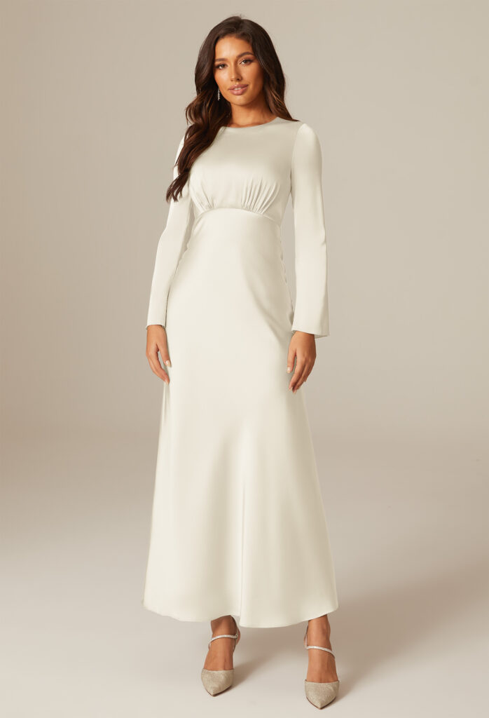 A woman wearing a long-sleeve, floor-length, cream-colored bridesmaid dress, posing against a neutral background.