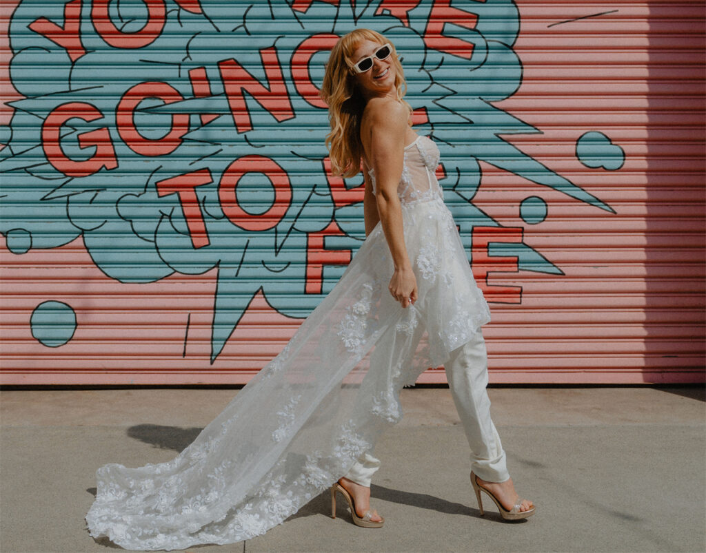 Bride wearing a short wedding dress with a long sheer overlay and sunglasses.