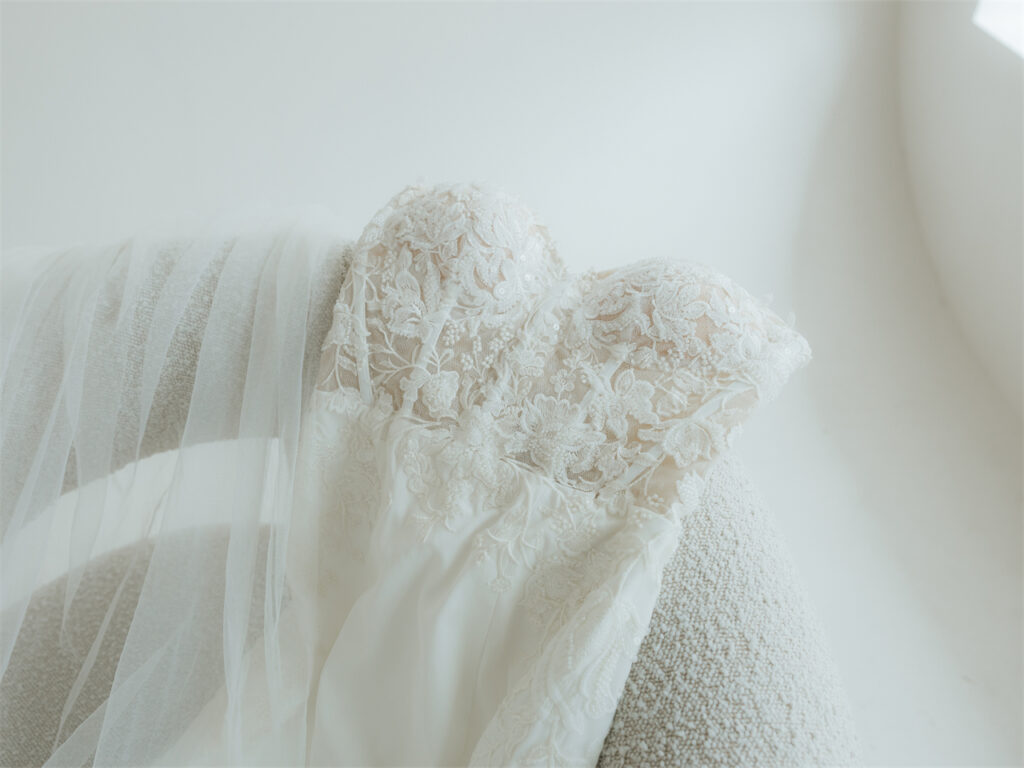 Close-up of a lace wedding dress draped over a textured chair.