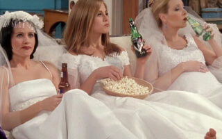 Monica, Rachel, and Phoebe from "Friends" sitting on a couch in wedding dresses.