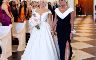 The bride and the mother of the bride walking down the aisle in a church, surrounded by guests.